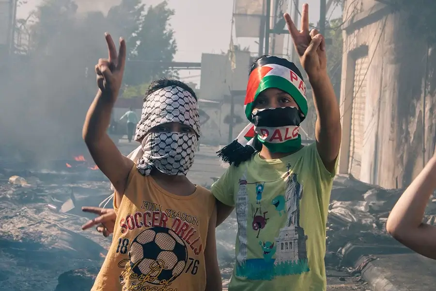 Två barn i palestinasjalar gör fredstecken med händerna i luften.